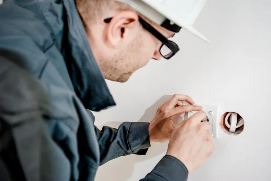 An electrician in safety glasses wiring a wall socket.