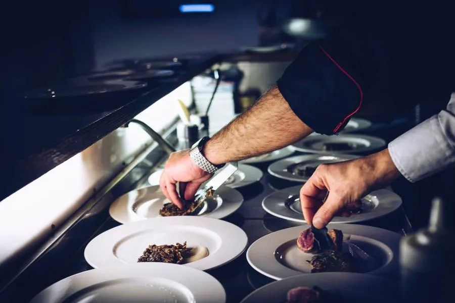 A chef plating a fine-dining dish in a professional kitchen.